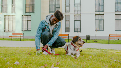 Casually dressed handsome guy collecting dog feces in plastic bag from green lawn near high...