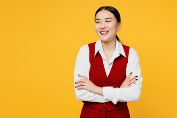 Young corporate lawyer employee business woman of Asian ethnicity wearing formal red vest shirt work at office hold hands crossed folded look aside isolated on plain yellow background. Career concept.