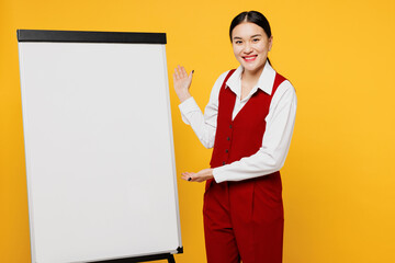 Young happy corporate lawyer employee business woman of Asian ethnicity wear formal red vest shirt work at office point on blank white board isolated on plain yellow background studio. Career concept.