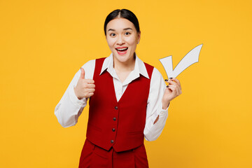 Young corporate lawyer employee business woman of Asian ethnicity wear formal red vest shirt work at office hold in hand check mark show thumb up isolated on plain yellow background. Career concept.