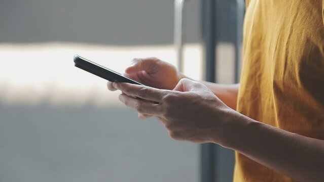 Silhouette of cropped shot of a young man working from home using smart phone and notebook computer, man's hands using smart phone in interior, man at his workplace using technology, flare light