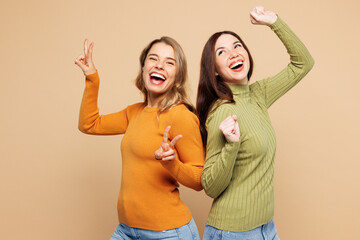 Young friends two women they wear orange green shirt casual clothes together do winner gesture show v-sign dancing isolated on plain pastel light beige background studio portrait. Lifestyle concept.