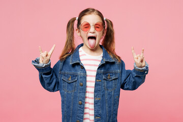 Little fun child cool kid girl 7-8 years old wears denim shirt glasses horns up gesture, depicting heavy metal rock sign isolated on plain pink background. Mother's Day love family lifestyle concept.