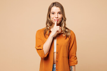 Young secret Caucasian woman she wear orange shirt casual clothes say hush be quiet with finger on lips shhh gesture isolated on plain pastel light beige background studio portrait. Lifestyle concept. - obrazy, fototapety, plakaty
