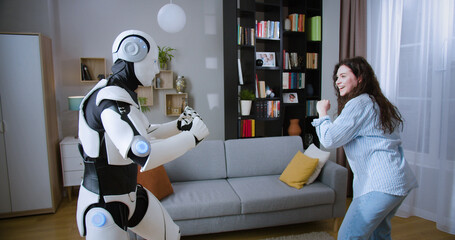 Caucasian woman imitating punches with humanoid cyborg while practicing boxing in living room....
