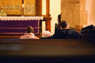 Rear view of a family sitting on the prayer seats inside a church