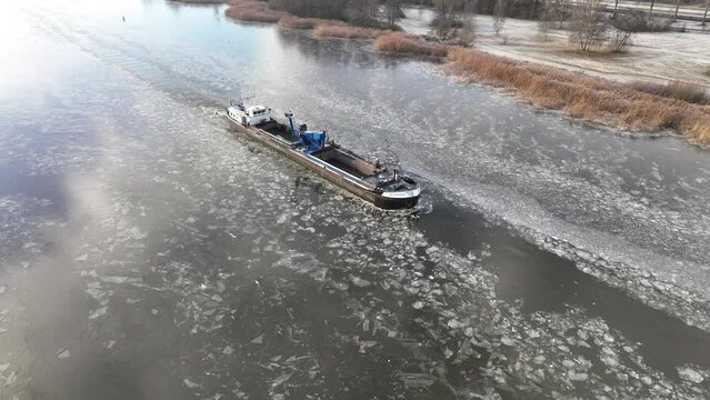 DRONTEN, NETHERLANDS - DECEMBER 14, 2022: Freight ship barge ploughing through ice on a froze Drontermeer lake during a cold winter day in The Netherlands