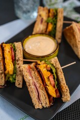 Vertical shot of a sliced appetizing club sandwich on a plate with sauce