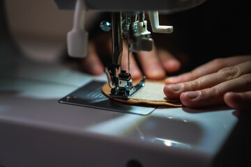 Close-up of a person sewing using a sewing machine, illuminated by a lamp