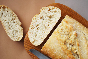 Wheat ciabatta on a board next to a knife on a brown-gray background