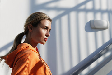 Young Woman Fitness Enthusiast Wearing an Orange Hoodie Resting Outdoors