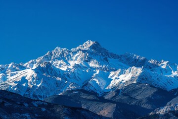 A view of a mountain range covered in snow under a clear blue sky, showcasing the rugged alpine landscape