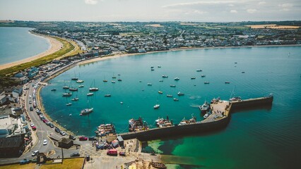 View of a harbor with a variety of boats in it, situated along the coast on a sunny day - obrazy, fototapety, plakaty