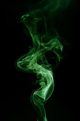 Fototapeta premium Swirling green smoke forms abstract shapes against a black background.