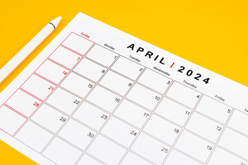 April 2024 desk calendar and pen on yellow color background.