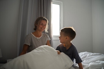 Happy mother and her little son cheerfully playing in the comfort of their bed