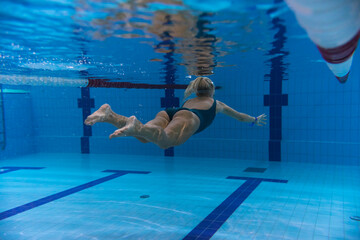 Underwater photography, a young blonde girl swims in a pool underwater, back view.