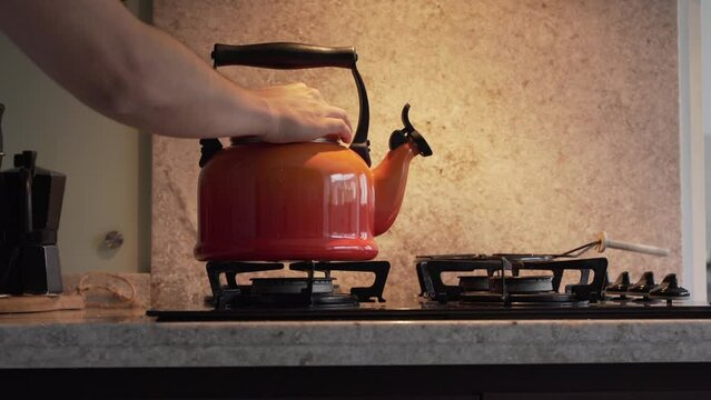 Hand secures the lid on an orange kettle on the stove