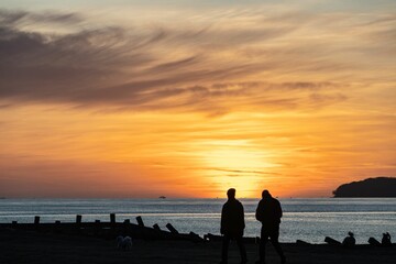 A silhouette of two people standing at the Lepe beach in front of a sunset