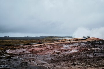 a boardwalk crosses a muddy road on a cloudy day, with steam vents in the