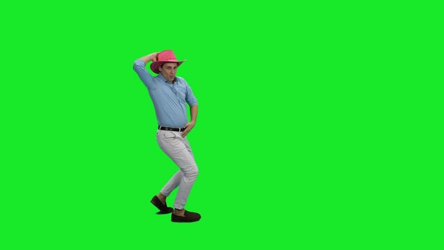 Young handsome slim man in white jeans blue shirt and red cowboy hat dancing on green background