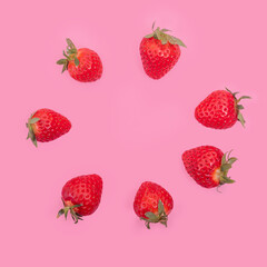 Whole ripe red strawberries are laid out in a circle on a pink background. Red ripe strawberries background.