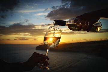 Pouring white wine into the glass against a breathtaking seaside sunset