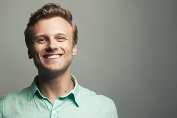 Male beauty, boy next door concept. Portrait of laughing 30-year-old man standing over gray...
