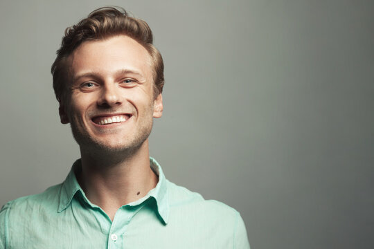 Male beauty, boy next door concept. Portrait of laughing 30-year-old man standing over gray background. Close up. Classic style. Wavy glossy blond hair. Copy-space. Studio shot