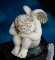 Small angel figurine with white wings and feathers is seated in a relaxed pose