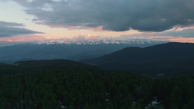 aerial view of a colorful sunset, forest and snowy mountains in the backgroun, drone travelling-in slowly moving forward