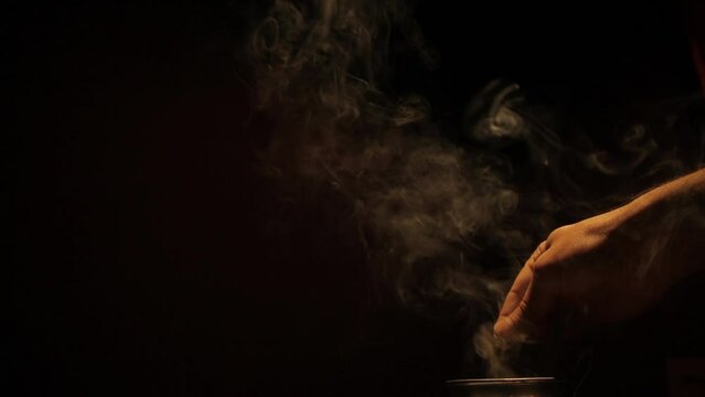 Closeup video of a person adding spices to hot pot on a black background