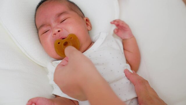 Asian mother gives a pacifier dummy to mouth infant baby girl on a bed. newborn baby sleeping home. Lifestyle newborn with a suck pacifier. Happy family kid dream concept. Pacifiers calm babies.