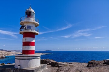 Faro de Arinaga lighthouse on the side of a hill with a blue sky in the background in Spain - Powered by Adobe