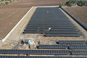 Aerial view of a large-scale solar farm with an array of black solar panels arranged in neat rows