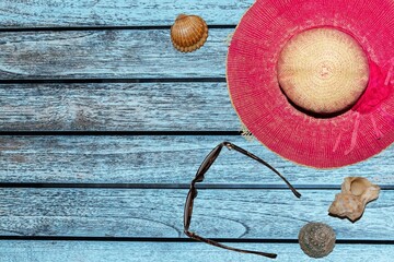 Sun hat with sunglasses and seashells on blue wooden background with copyspace