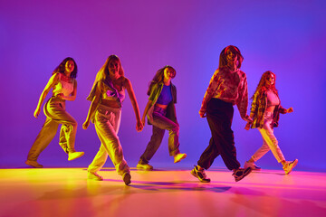 Dynamic image of young talented women in casual clothes in motion, dancing street style dance against gradient background in neon. Concept of youth, street dance, contemporary dance, modern, dynamics