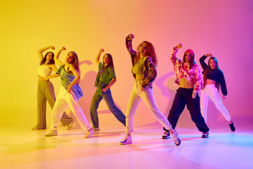 Artistic, talented young women in motion, dancing street style dance against gradient background in neon light. Concept of youth, street dance, contemporary dance, modern, dynamics