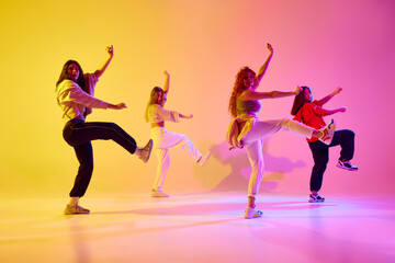 Beautiful young women, dancers in motion in casual clothes dancing against gradient background in...