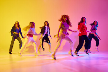 Talent show. Young women, group of artistic female dancers, woman performing streetstyle dance against gradient background in neon. Concept of youth, street dance, contemporary dance, modern, dynamics