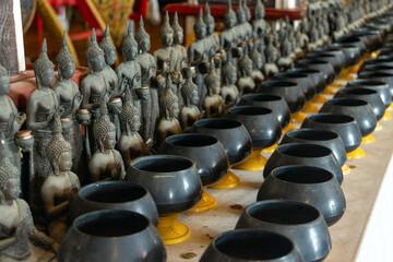 Rows of Buddha figures with long rows of coin bowls inside a Buddhist temple, Thailand