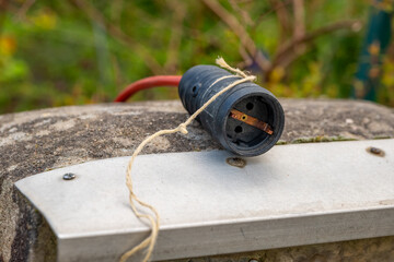 black electrical plug with a red cord tied to it