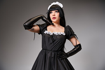 attractive young cosplayer in maid costume posing alluringly and looking away on gray backdrop