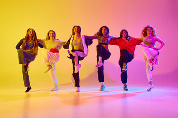 Young talented, beautiful women dancing hip hop, contemp, freestyle against gradient background in neon light. Concept of youth, street dance, contemporary dance, modern, dynamics
