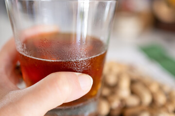Hand holding a glass of fresh beer with peanuts on a table with a blurred background.