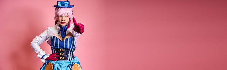 chic female cosplayer in vibrant dress with blue hat pointing at camera on pink backdrop, banner