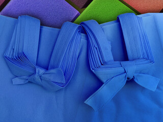 pile of two packs of porous blue tote bags. non-woven fabric tied with rope. polypropylene bag on multicolored checkered background