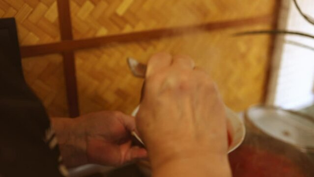 grandmother's hands with a ladle pour borscht red soup into a white plate over the stove in the kitchen. Grandma is cooking borscht