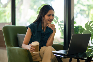 Happy young woman takes a break from work to drink coffee and chat with people through her laptop camera in a coffee shop.