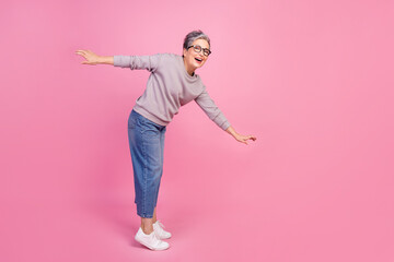 Full length photo of funky cheerful senior woman wearing trendy clothes standing balancing empty space isolated on pink color background